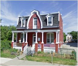 Exterior view of the small, two-storey red brick artists' studio with white trim.